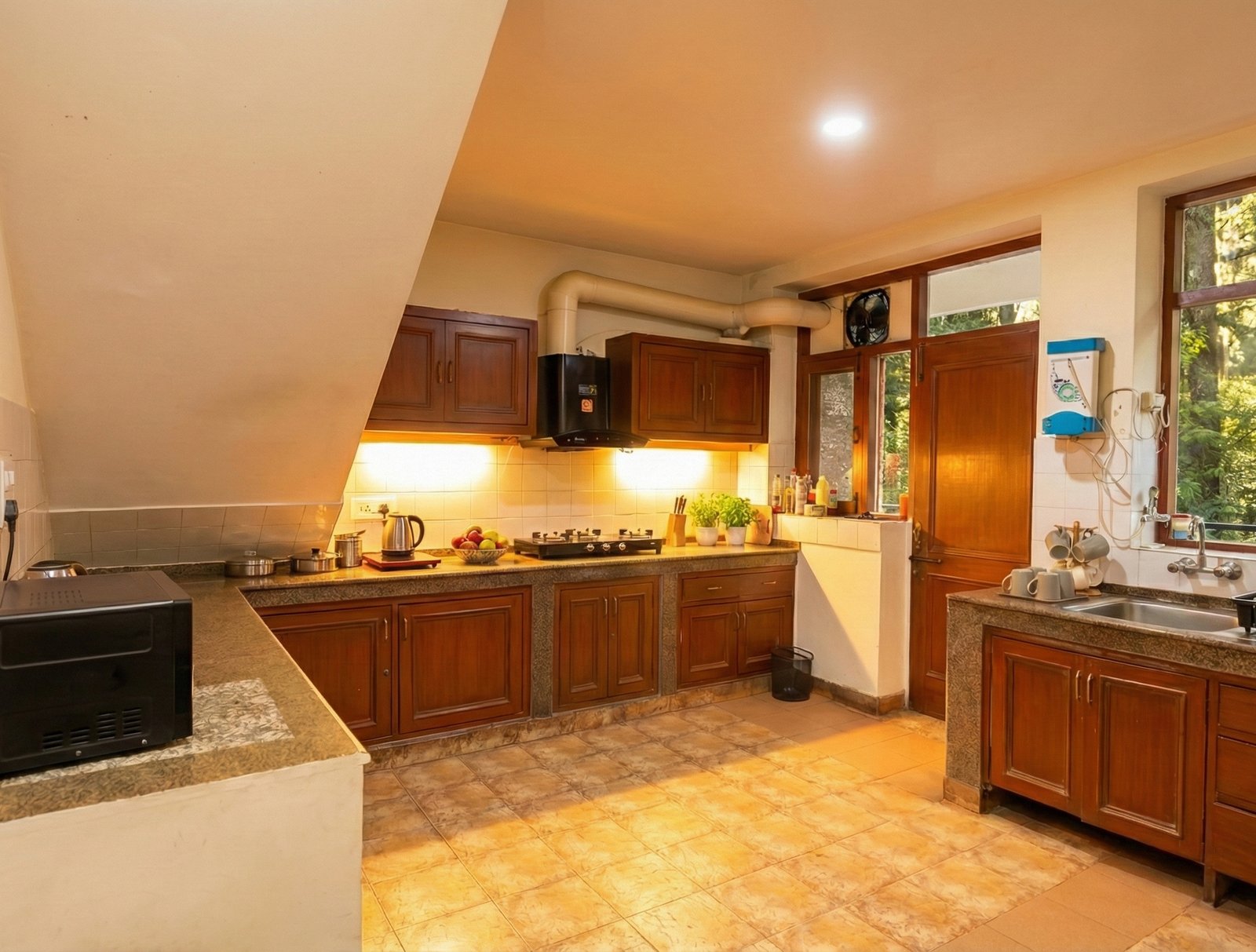 Fully equipped modern kitchen with gas stove, refrigerator, and ample counter space for preparing meals at Forestbound Cottage Manali